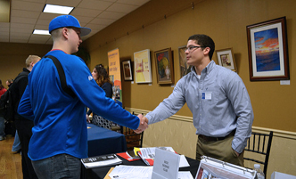 Student shaking hands with a person behind during a career fair.