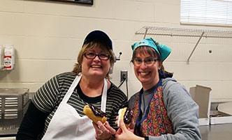 Two women in the culinary lab, holding homemade eclairs.