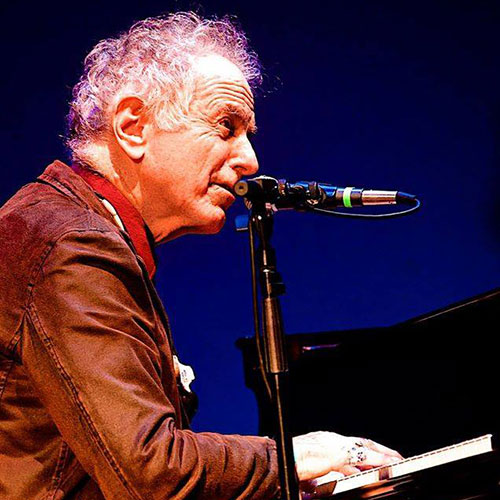 David Amram playing a piano and singing into a microphone.