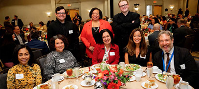 A group of College official sit around a table with plated salads. 