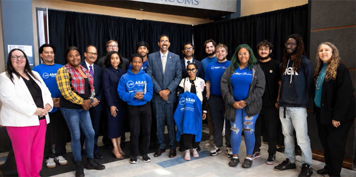 College officials and students blue ASAP tee shirts stand together in a group posing for an image. 