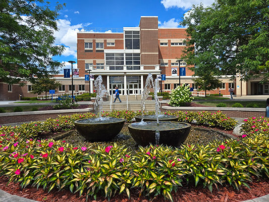 The fountain in the Quad at SUNY Schenectady, surrounded by flowers. Stockade Building in the background.