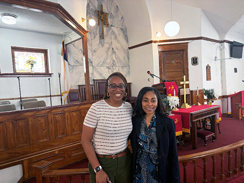 Two Black women stand at the alter in a church.