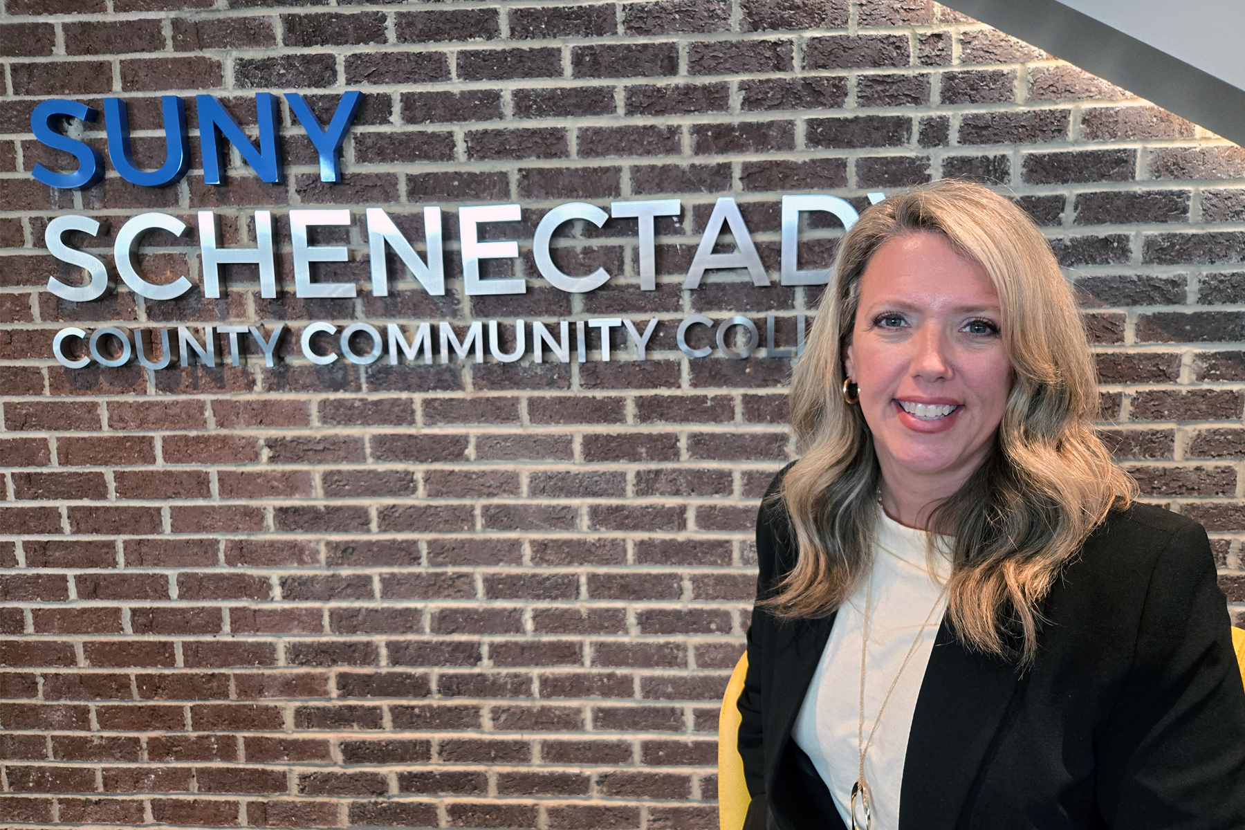Christina Charette seated in front of SUNY Schenectady sign