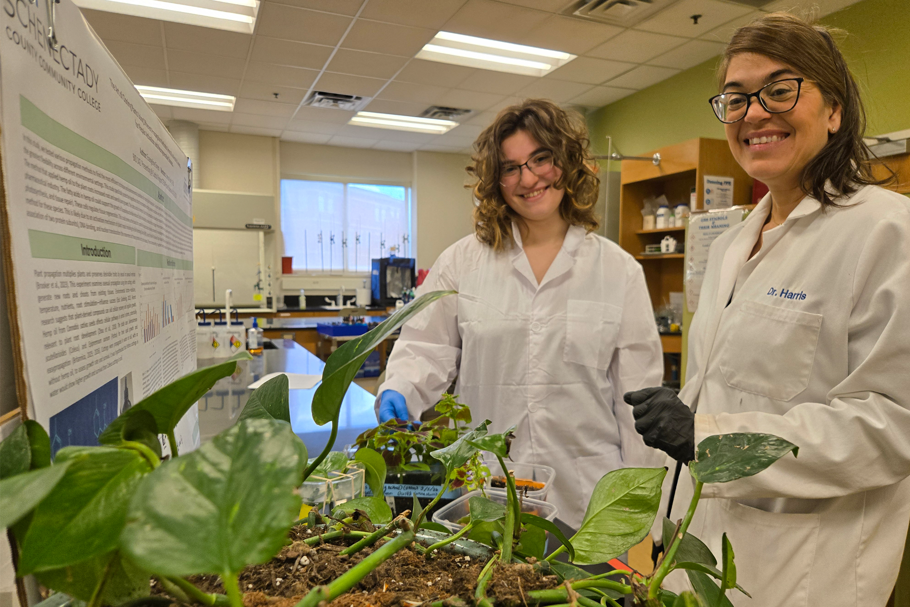 Evangeline Green and Dr. Lorena Harris wearing lab coats in Science Lab, with plants in front of them