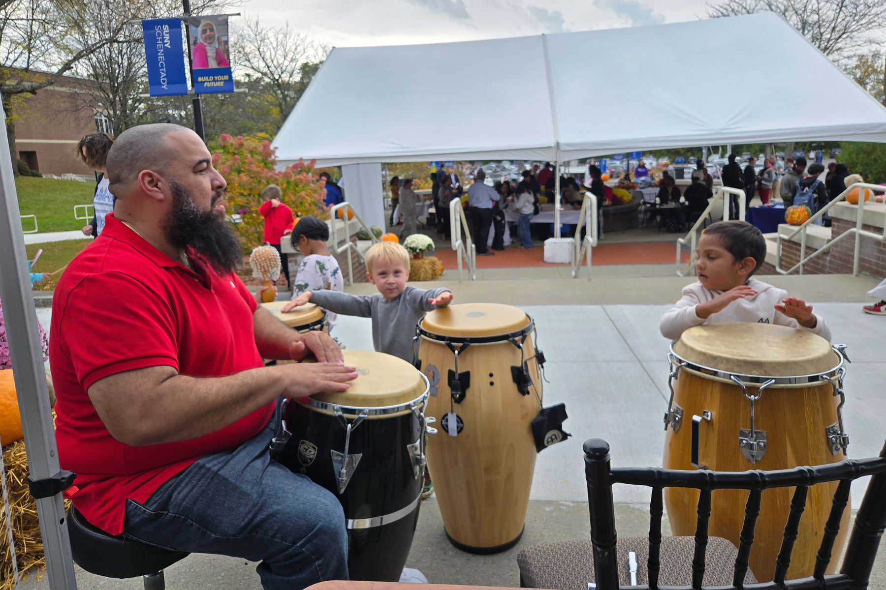 Kids playing the drums with drummer outside in the Quad at Harvest Fest. 