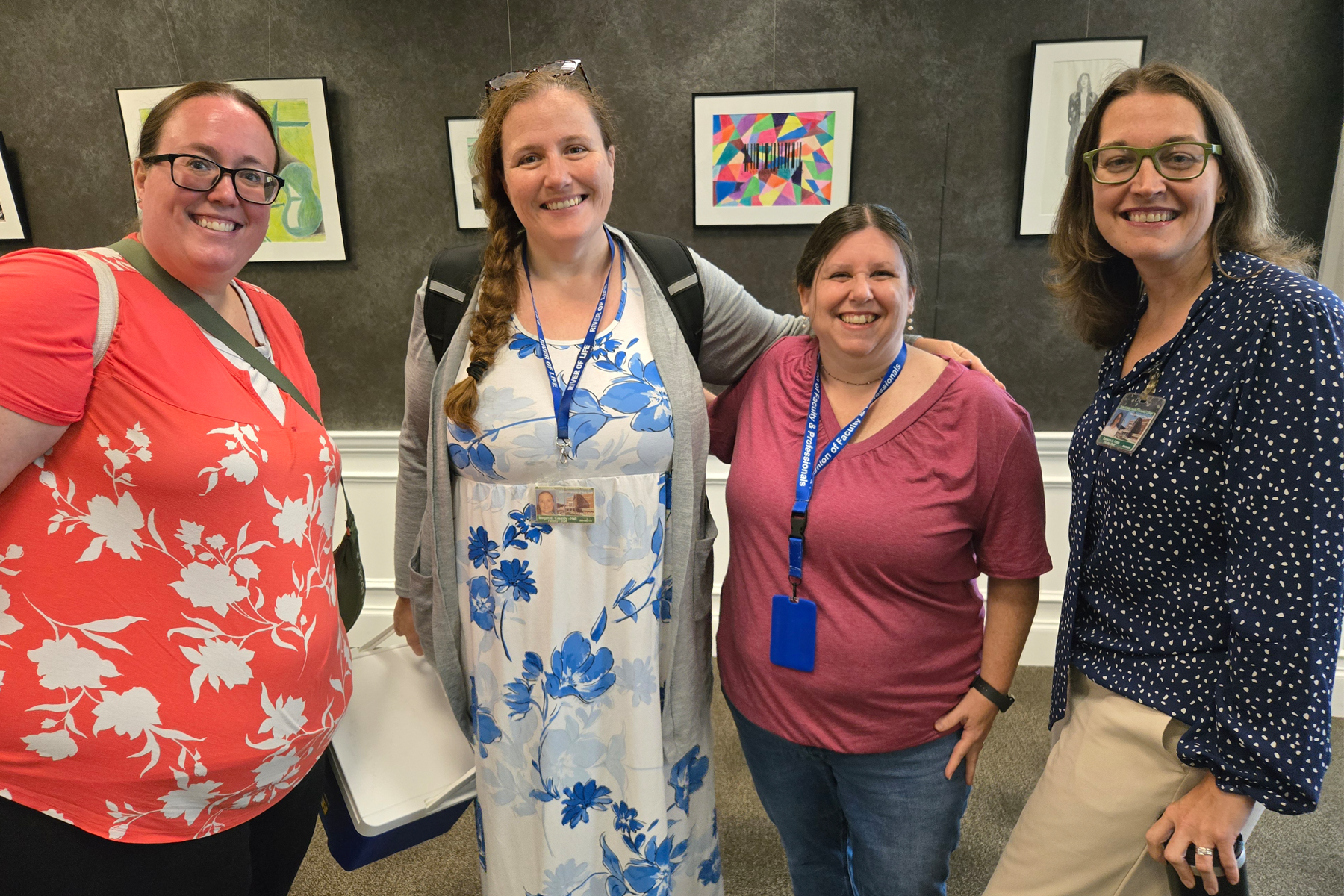 Four faculty members, smiling, standing in Casola Dining Room