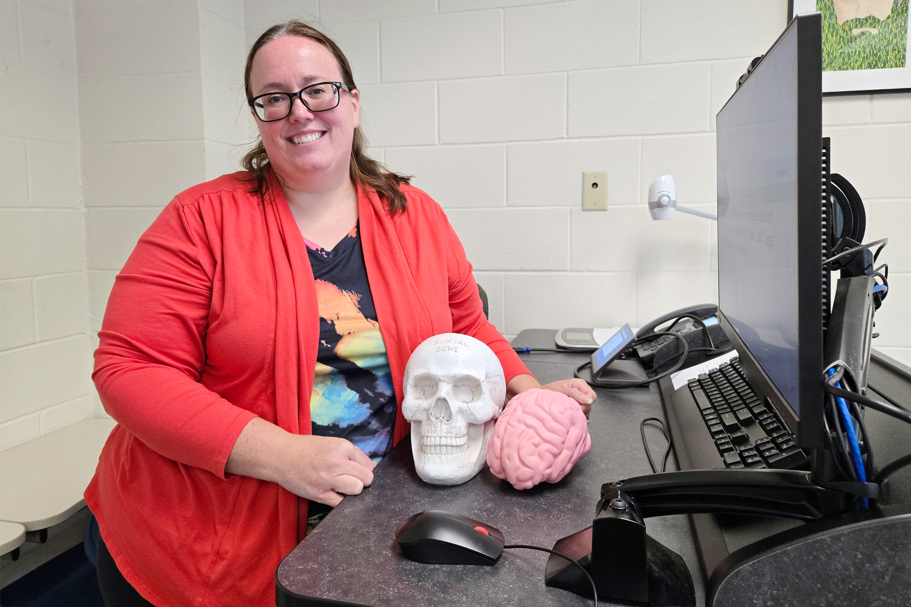 Dr. Melissa Evans, standing at professor's podium at front of classroom, smiling