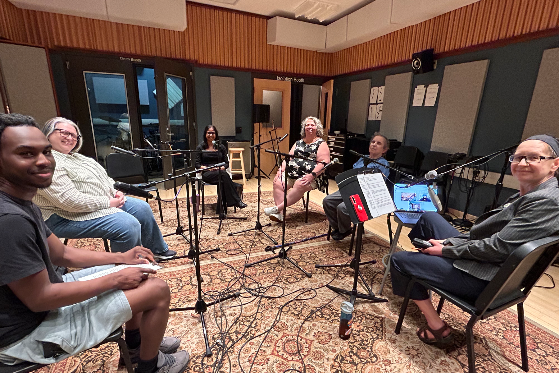 Co-hosts and guests sitting in recording studio, with microphones in front of them