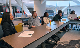 Dr. Reaves sits at a table with several students, intently listening.