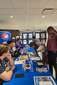 Students standing at a staffed table, asking questions.
