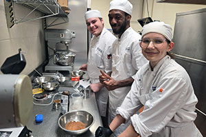 Three culinary students standing together at a counter in the kitchen working on a recipe.
