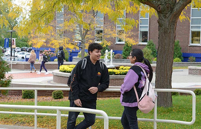 Two students leaning on the walkway railing in the Quad, chatting. 