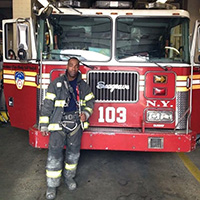 Kendall Richardson in his fire fighter's gear, standing in front of a fire truck.