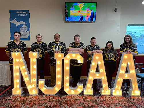 Bowling team in front of large NJCAA light up sign in 2024.