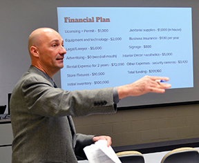 Professor Matt Farron in front of a class, with a financial breakdown of a business on screen behind him.