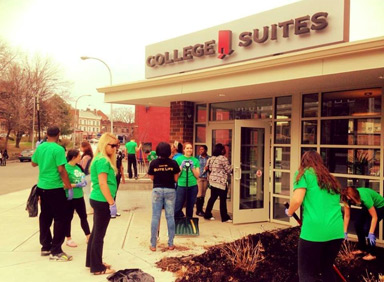 Students outside the entrance of College Suites at Washington Square, all wearing matching tee shirts, doing a fall clean up.