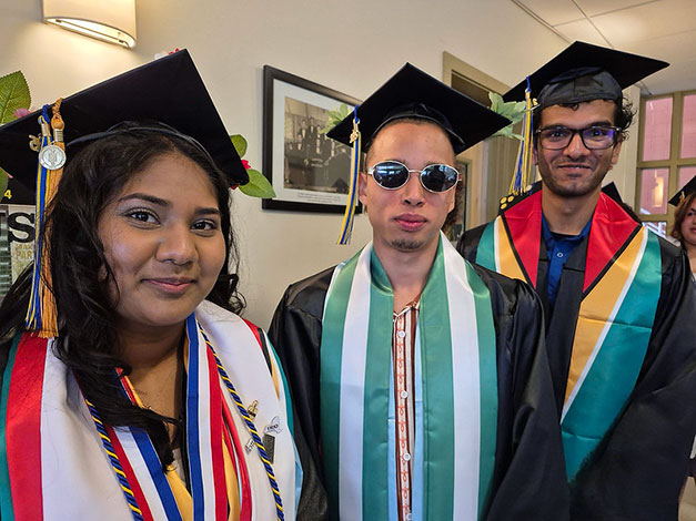 Three 2025 graduates standing together in their caps and gowns. 