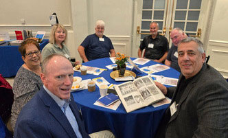 Group of alumni sit around a table looking at College yearbooks. 