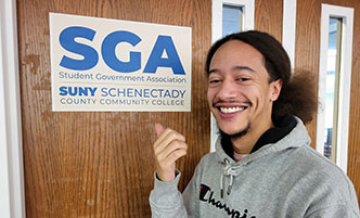 SGA member standing in front of the SGA Office sign.