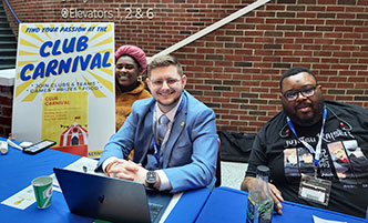 Three students behind a table at a student activities fair.