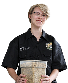 Female student in black, short sleeve button up shirt, holding a container of hops for beer brewing.