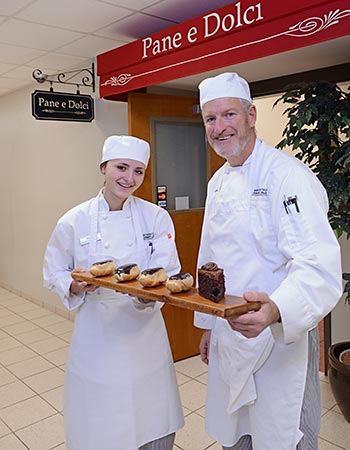 Culinary student holding a trays of bakery treats in front of Pane e Dolci.