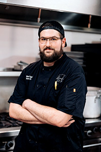 Chef Nick Gabriel, wearing a black chef coat, standing in a restaurant kitchen.
