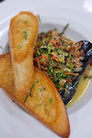 Mussles topped with bacon and greens, with a side of toasted bread.