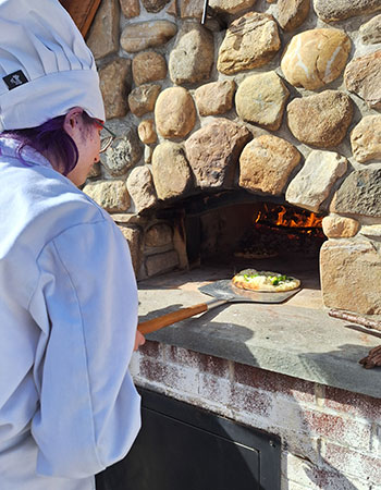 Culinary student putting a pizza into the brick oven.