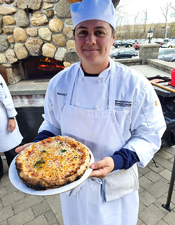Culinary student holding a finished brick-oven cooked pizza.