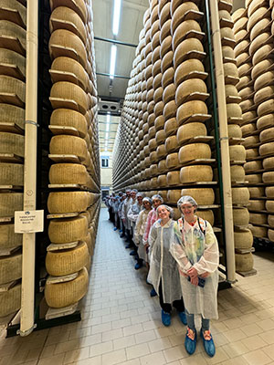 SUNY Schenectady culinary students lined up in a Parmesan aging facility in Italy. Cheese towers to the ceiling.