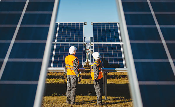 Two technicians in safety gear inspect gound-mounted solar panels.