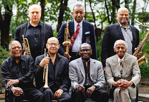Seven members of the Cookers, all wearing suits, four members holding instruments.