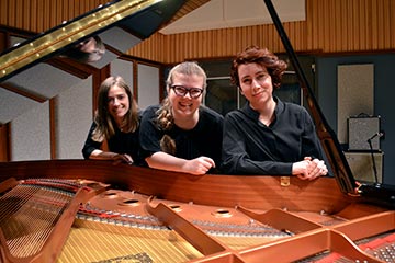 Niamh Paris, Iida Nyman and Rebecca Schmid looking through the lid of a grand piano.