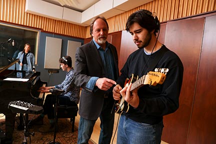 Sten Isachsen working with a guitar student in SUNY Schenectady's recording studio. Other students working in the background. 