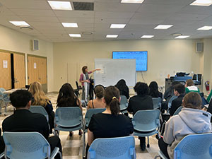 Music faculty member at a white board, students sitting in chairs all around.