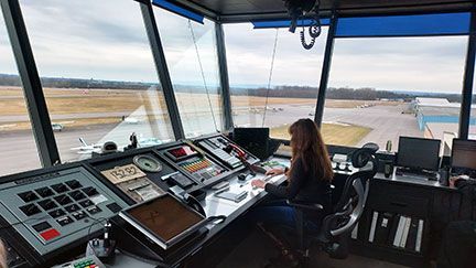 Student working inside the Control Tower at Schenectady Airport, airplane visible on the ground outside the windows. 