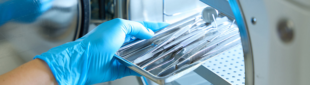 Gloved hand holding a tray of sterile medical instruments.