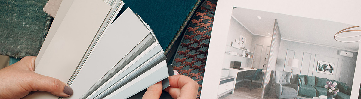 Close up of a hand holding paint swatches above fabric samples and a printout image of a room.