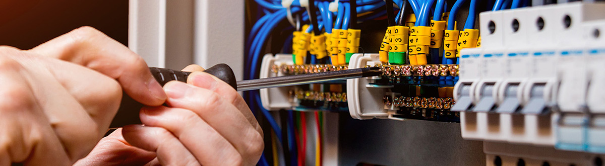 Close up of someone's hands holding a screwdriver, working inside an electrical panel box.