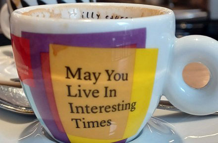 Close up of a coffee cup with the words, May You Live In Interesting Times, written on it. 