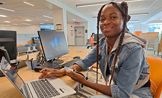 Woman working on a laptop, holding a cell phone. 