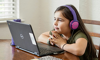 Young girl wearing purple and pink headphones, looking at a laptop.