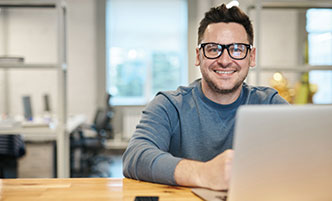 Man wearing glasses, sitting in front of a laptop.