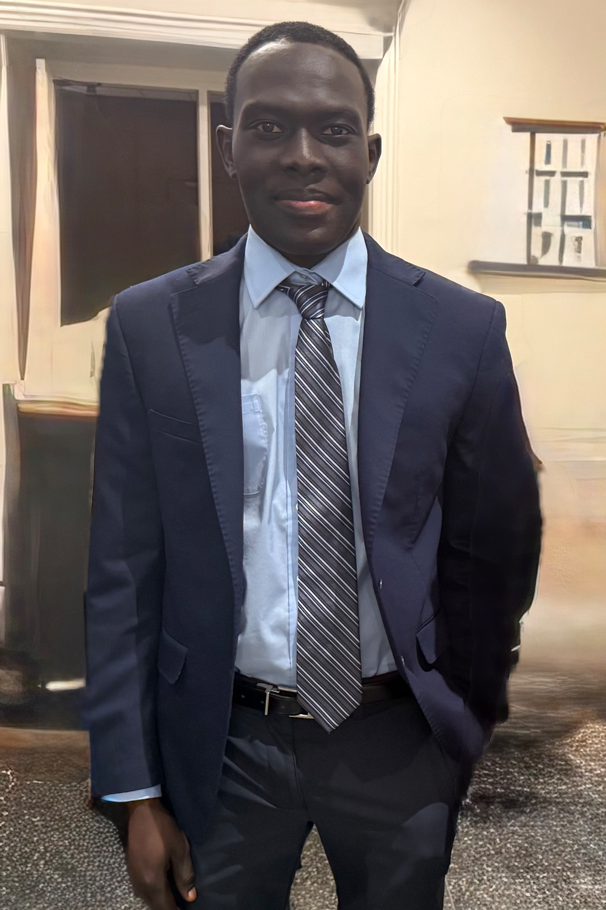 Altahi Akbar wearing suit and tie, standing and smiling