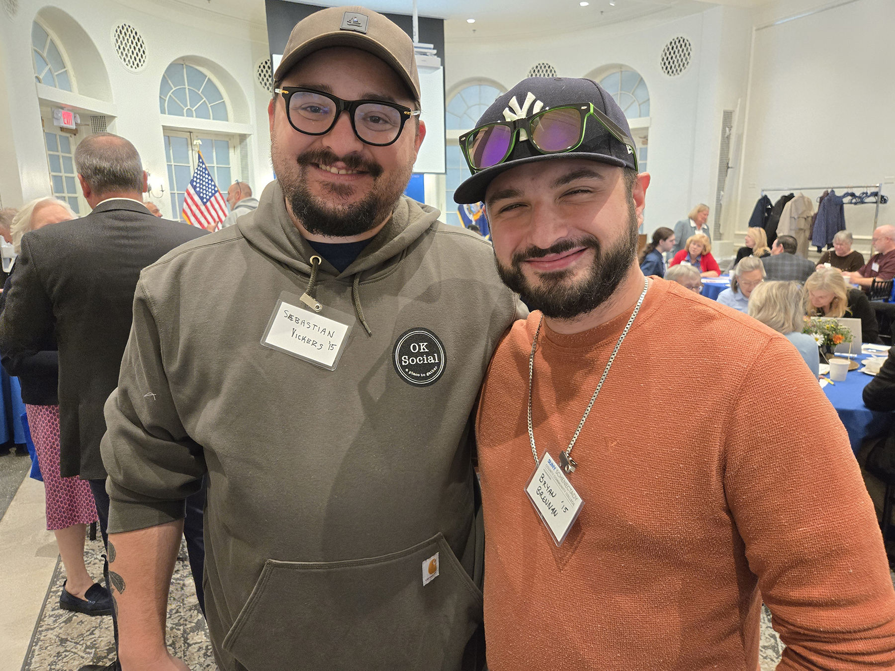 Two alumni standing in Lally Mohawk Room, smiling