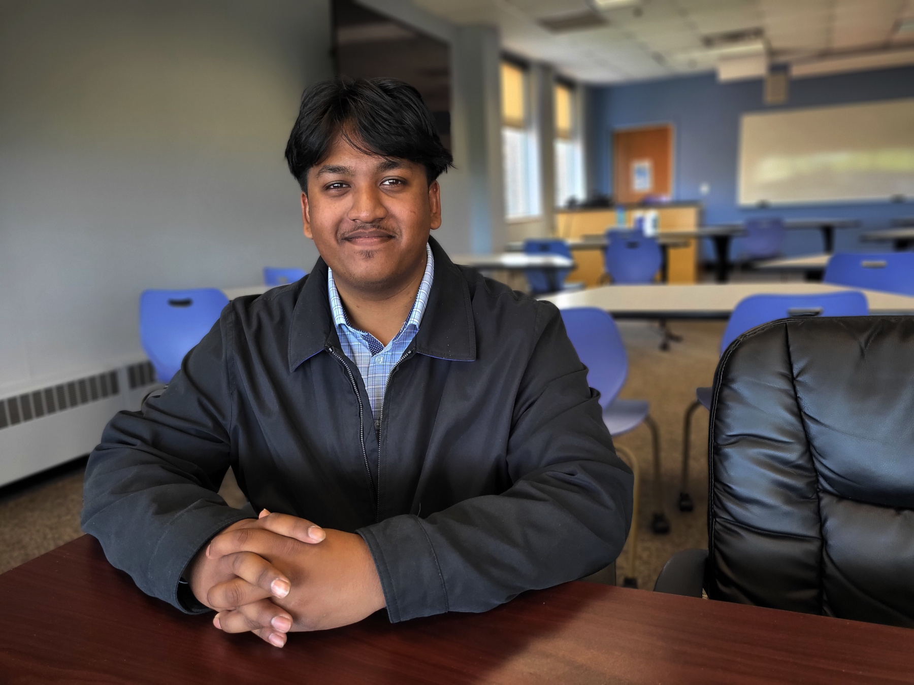 Anthony Bisnauth sitting at table in Business Classroom, smiling