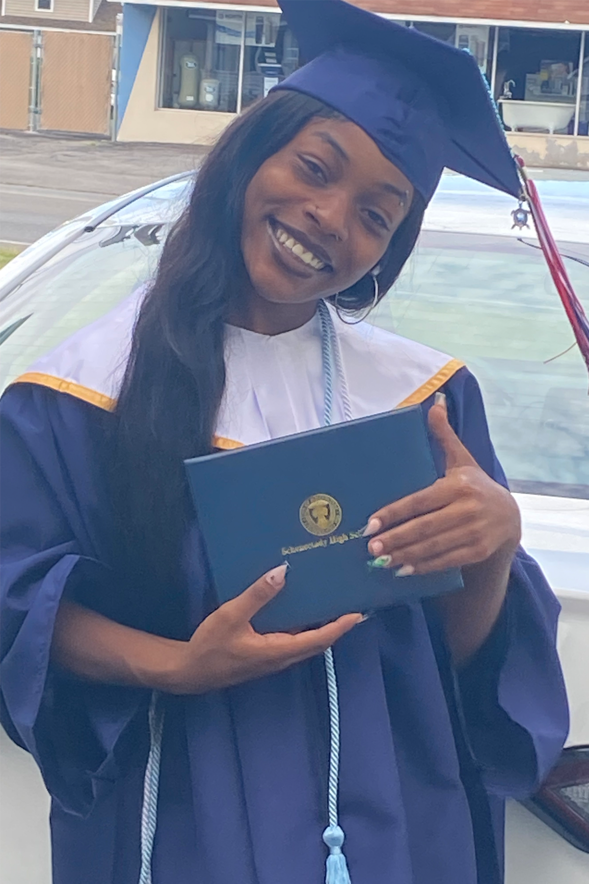 Brook-Lynn Winston, standing in cap and gown, holding diploma