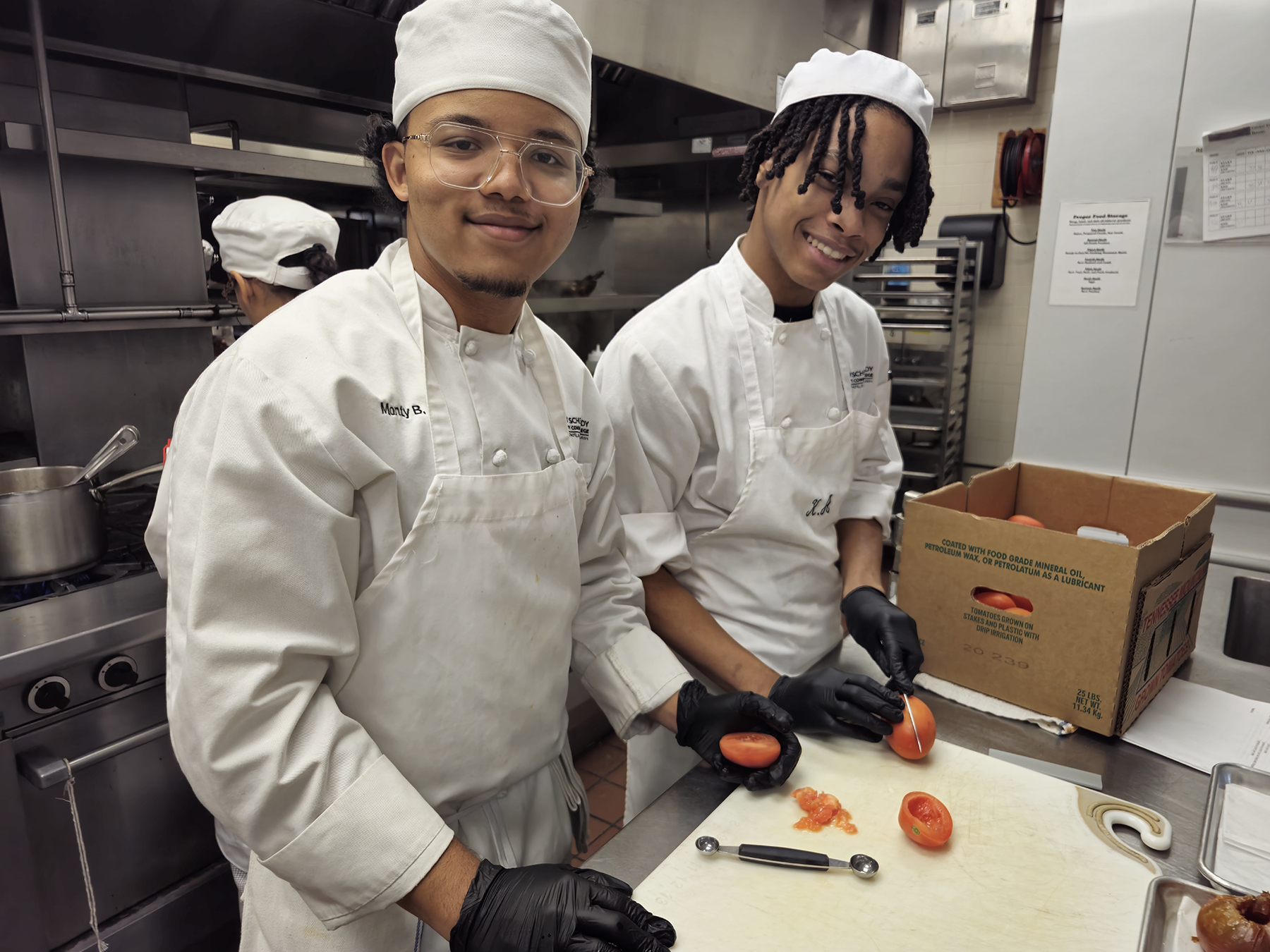 Two student chefs cutting tomatoes in kitchen